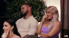a woman in a purple dress is covering her mouth while a man sits behind her