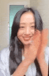 a woman with long black hair is smiling and clapping her hands in a room .