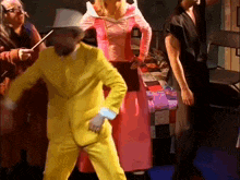 a man in a yellow suit is dancing in front of a group of people dressed in costumes .