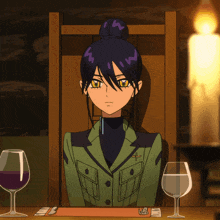a woman in a green jacket sits at a table with two wine glasses and a candle