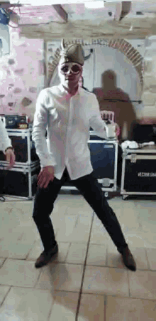 a man wearing a hat and sunglasses is dancing on a tiled floor in a room .