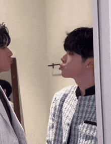a man with a cigarette in his mouth looks at another man in front of a mirror