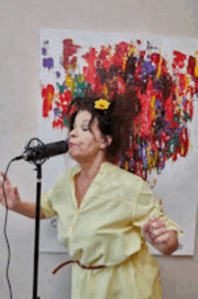 a woman in a yellow dress is singing into a microphone in front of a painting