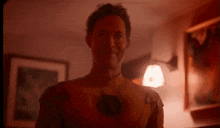 a man in a superhero costume is smiling in a dark room with a lamp in the background .
