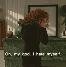 a woman is standing in front of a fireplace with her hands on her head and says oh my god i hate myself