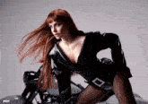 a woman with long red hair is standing next to a motorcycle with mm written on the bottom right