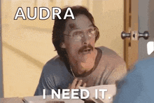 a man with glasses and a mustache is sitting at a table and says audra i need it .