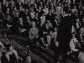 a man in a tuxedo stands in front of a large crowd of people