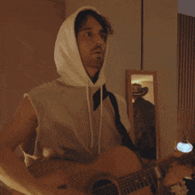a man wearing a hoodie is holding a guitar