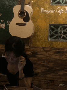 a woman sits at a table in front of a guitar and a sign that reads bonjour cafe