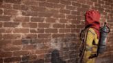 a person wearing a red hood and a yellow jacket is standing in front of a red brick wall