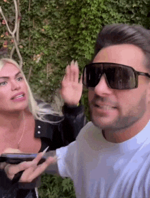 a man wearing sunglasses talks to a woman while holding a cell phone