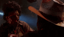 a man in a cowboy hat is holding another man 's hand with blood on it