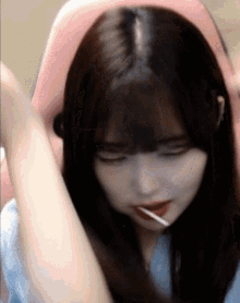 a girl with long hair is sitting in a pink chair with her eyes closed and a lollipop in her mouth .