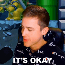 a man sitting in front of a microphone with the words " it 's okay " written below him