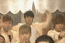 a group of young men are standing in front of a microphone and pointing at something