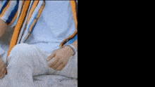 a man in a striped shirt and white pants is sitting down with his legs crossed .