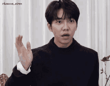 a man in a black sweater is making a funny face with his hand in the air