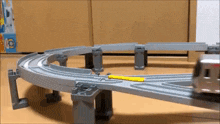 a toy train is going down a curved track with a yellow object in the middle
