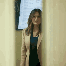 a woman in a tan suit is standing in front of a large screen .