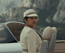a woman wearing a hat is standing in front of a car