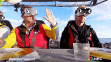 two men wearing virtual reality glasses are sitting at a table eating