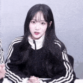 a girl with long black hair wears a black and white striped jacket