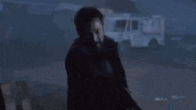a man in a black coat is standing in front of a white truck in the dark .