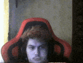 a man wearing headphones sits in a red gaming chair
