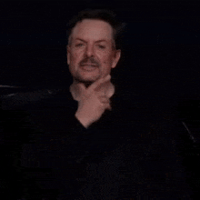 a man with a beard is making a funny face in a dark room while wearing a black shirt .