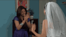 a woman in a purple dress and a bride in a white veil are clapping hands