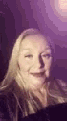 a close up of a woman 's face in a dark room with purple lights behind her .
