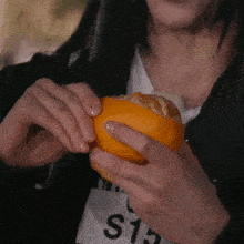 a woman is holding an orange in her hands with s13 on her shirt