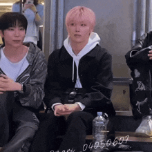 a man with pink hair sits next to a bottle of water