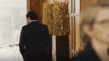 a man in a suit is walking down a hallway with a statue in the background .
