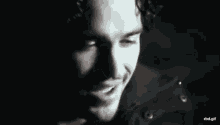 a man with curly hair is smiling in a black and white photo with his mouth open .