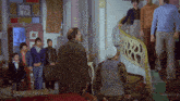 a group of people are standing in a room with a staircase leading up to the second floor