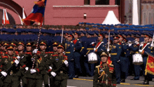 a group of soldiers marching in front of a building with a flag behind them