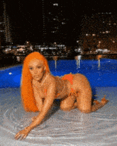 a woman in an orange bikini is kneeling in a swimming pool at night .
