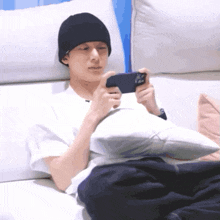 a man wearing a black beanie is laying on a couch playing a game on his phone