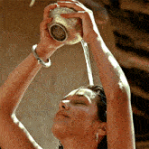 a woman is pouring water from a silver bowl over her head