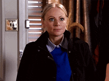 a woman wearing a black jacket and a blue sweater is standing in front of a door .