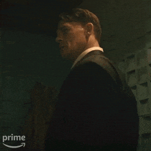 a man in a suit and tie is standing in a dark room with a prime logo in the corner