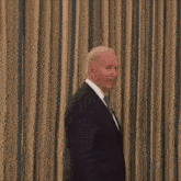 a man in a suit and tie is standing in front of a curtain and smiling .