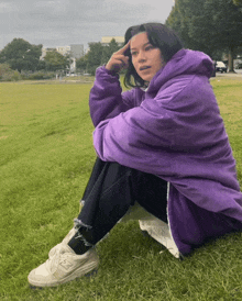 a girl in a purple jacket sits on the grass