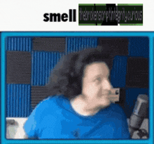 a man in a blue shirt is standing in front of a microphone with the words smell written above him