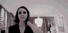 a woman in a black dress is standing in a living room with a chandelier .