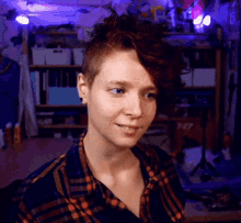 a woman with a shaved head and a plaid shirt looks at the camera