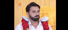 a man with a beard and a garland around his neck is wearing a white shirt .