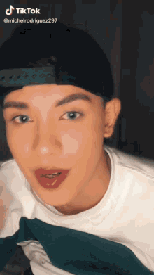a young man wearing a baseball cap and a white shirt has a tiktok sticker on his face